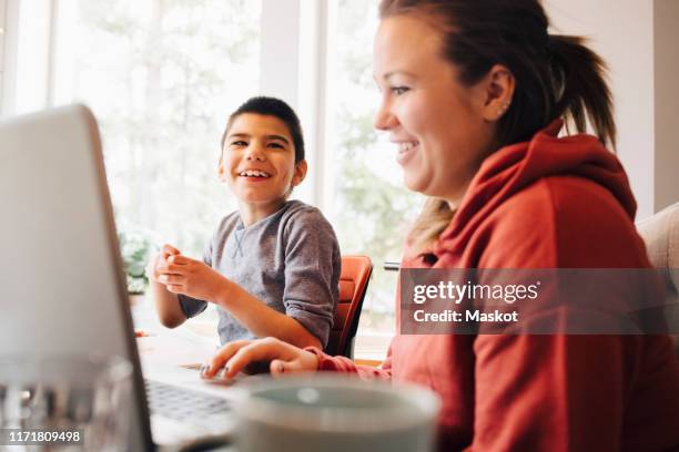 mother using laptop while sitting with happy autistic son in living room at home - autistic adult imagens e fotografias de stock