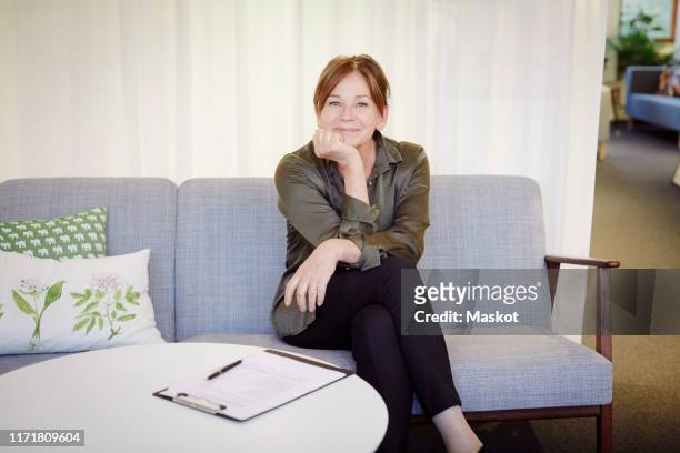 portrait of confident smiling female psychologist sitting on sofa at workshop - mental health professional stock pictures, royalty-free photos & images