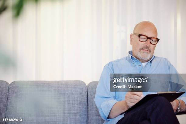 confident senior therapist writing on clipboard at wellness center - psychiatrists couch fotografías e imágenes de stock