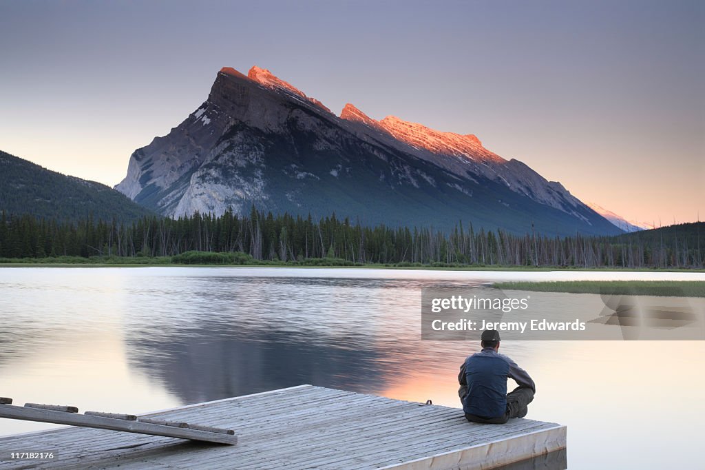 Man sitting on edge of dock by Mount Rundle, Banff