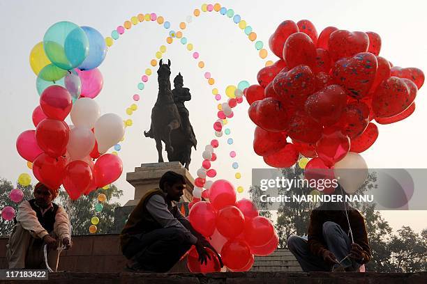 Indian labourers Bharat Kurli, Sunil Gupta and Sati Ram hold balloons by the statue of Maharaja Ranjit Singh at Ram Bagh garden in Amritsar on...