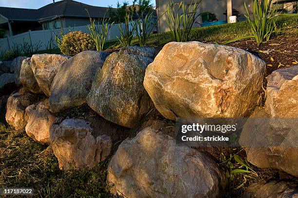 filtered golden sunlight iluminates rock retaining wall - boulder retaining wall stock pictures, royalty-free photos & images