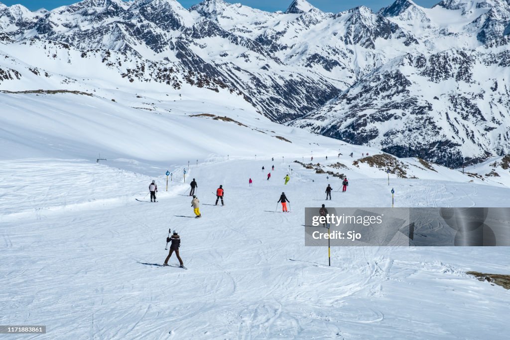People skiing and snowboarding down a ski slope in the Sölden Ötztal ski area during a sunny winter day