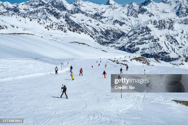 people skiing and snowboarding down a ski slope in the sölden ötztal ski area during a sunny winter day - sölden stock pictures, royalty-free photos & images