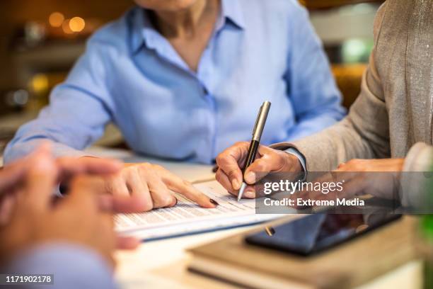 compañero de trabajo más joven señalando a su colega mayor la línea de firma en un documento durante una reunión - encoger fotografías e imágenes de stock