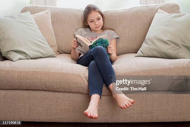 young girl reading book on sofa - barefoot stock pictures, royalty-free photos & images