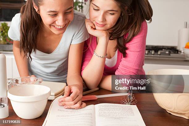 teenage girls looking at recipe in kitchen - baking reading recipe stockfoto's en -beelden