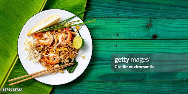 weltberühmte thai ische rezept von garnelen pad thai nudeln mit essstäbchen auf einem gericht und bananenblatt auf einem türkisfarbenen alten holztafel tisch hintergrund. - thailändische küche stock-fotos und bilder