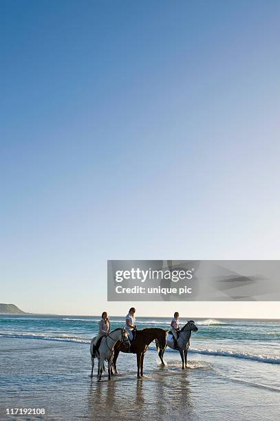3 people riding horses on the beach - horse riding group stock pictures, royalty-free photos & images
