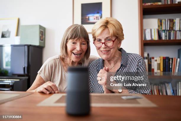 excited senior friends using a smart speaker - cream colored shirt stockfoto's en -beelden