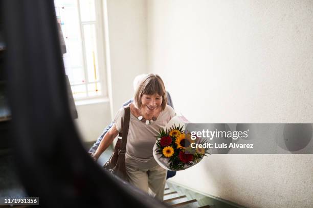 senior woman walking up the stairs with flowers - beklimmen stockfoto's en -beelden