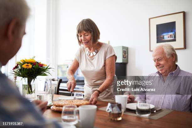 senior woman serving food to friends at home - party pies foto e immagini stock