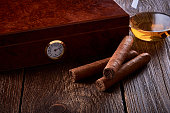 Still life with wooden box for humidification, three cigars and glass of whiskey on old table.