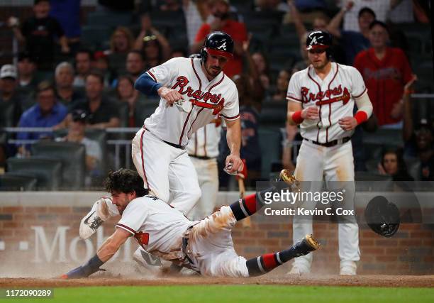 Dansby Swanson of the Atlanta Braves slides safely across home plate into Matt Joyce as they and Josh Donaldson score on a three-RBI double by Tyler...