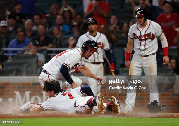 Dansby Swanson of the Atlanta Braves slides safely across home plate into Matt Joyce as they and Josh Donaldson score on a three-RBI double by Tyler...