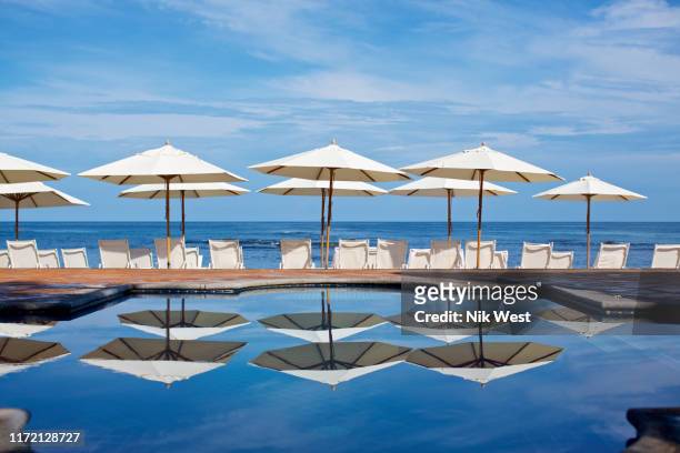 white beach umbrellas and lounge chairs at sunny ocean poolside, punta de mita, nayarit, mexico - resort pool stock-fotos und bilder