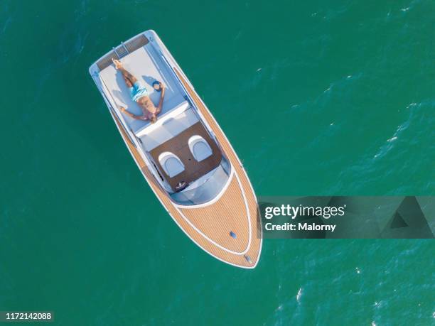 aerial view of motor boat floating on a lake. young man sun bathing on deck. - motorboot stock-fotos und bilder