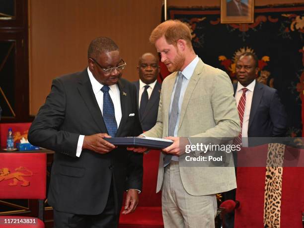 Prince Harry, Duke of Sussex presents Professor Arthur Peter Mutharika, President of the Republic of Malawi with a gift at the State House on day...