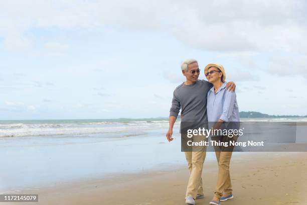 seniors taking on the world, modern healthy 60 year old couple on beach walk - asian couple walking stock pictures, royalty-free photos & images