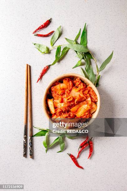 Korean traditional fermented appetizer kimchi cabbage salad in ceramic bowl with shopsticks and Vietnamese oregano greens over grey spotted...