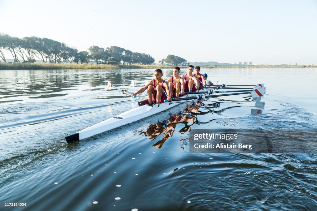 Mixed race rowing team training on a lake at dawn