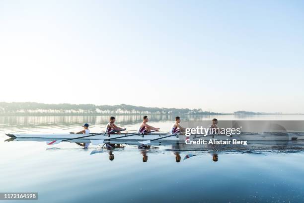mixed race rowing team training on a lake at dawn - dedicación fotografías e imágenes de stock