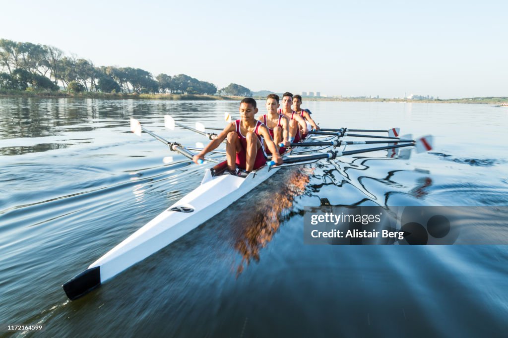 Mixed race rowing team training on a lake at dawn