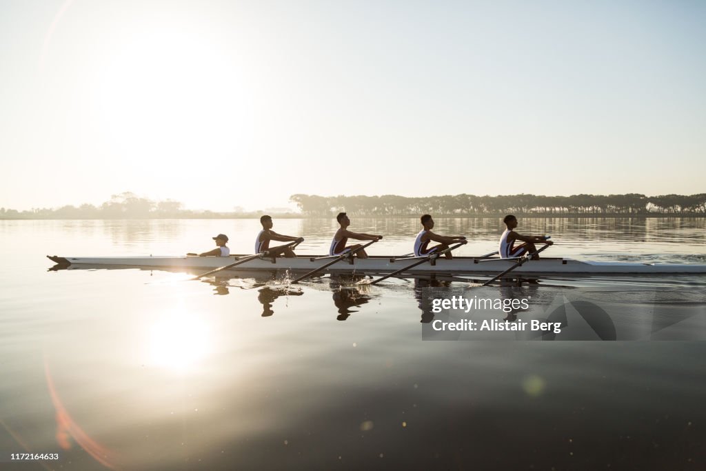 Mixed race rowing team training on a lake at dawn