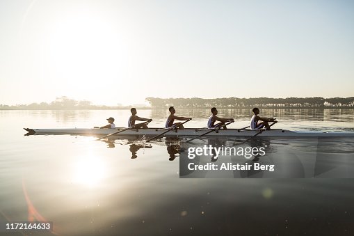 Mixed race rowing team training on a lake at dawn Mixed race rowing team training on a lake at dawn