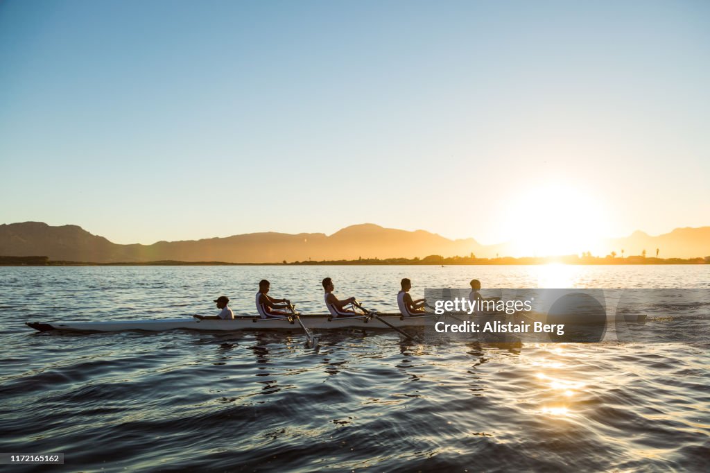 Mixed race rowing team training on a lake at dawn