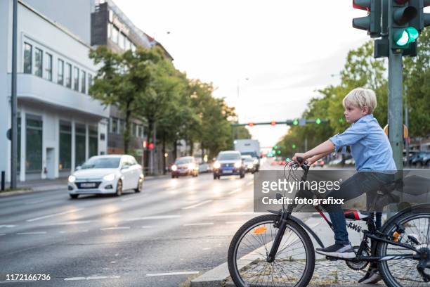 boy with bicycle is waiting at the traffic light of a big road - traffic crossing stock pictures, royalty-free photos & images
