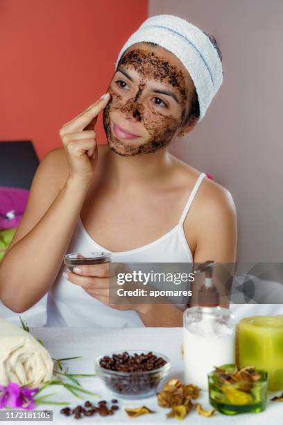 jeune femme hispanique avec le gommage de visage de café après le bain regardant l'appareil-photo. exfoliation de la peau. - laver en frottant photos et images de collection