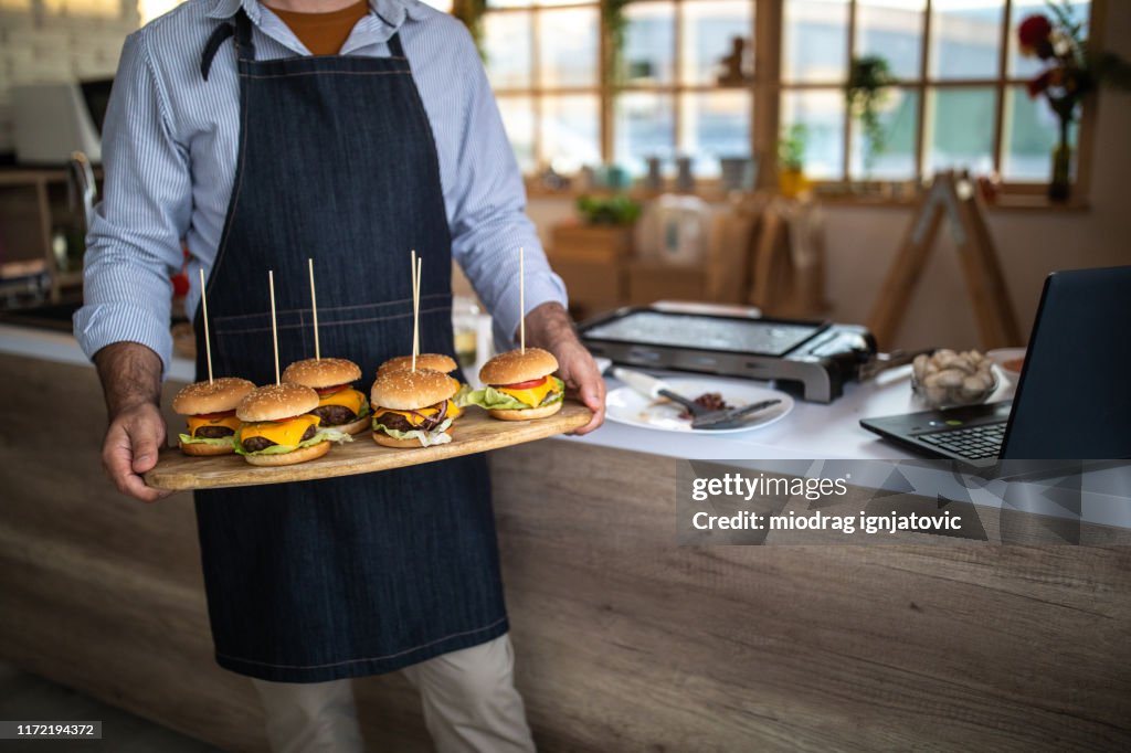 Hands holding a big wooden plate with homemade gourmet slider-burgers