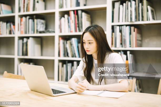 serieuze vrouwelijke student met laptop in bibliotheek - taiwanese ethnicity stockfoto's en -beelden