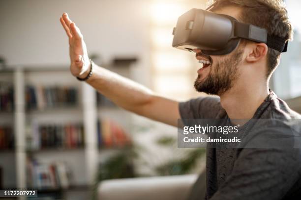 jeune homme utilisant le casque virtuel de simulateur de réalité à la maison - casques réalité virtuelle photos et images de collection