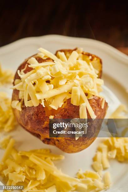 baked potato sliced open filled with grated cheddar cheese served on a white plate. - baked potato stock pictures, royalty-free photos & images