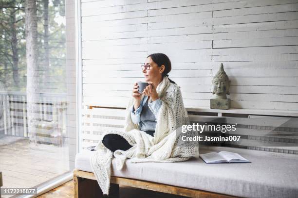 vrouw zit comfortabel en kijkt door het raam - mature woman winter stockfoto's en -beelden