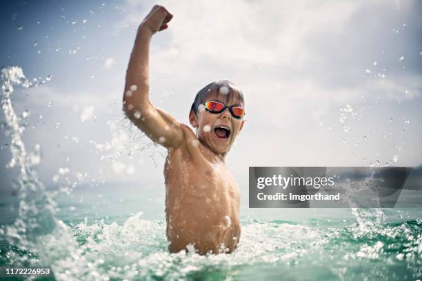 niño jugando y salpicando en las olas del mar - niño bañandose fotografías e imágenes de stock