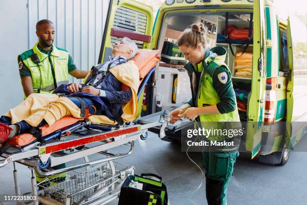 paramedic with patient looking at coworker preparing oxygen equipment outside ambulance - stretcher ストックフォトと画像