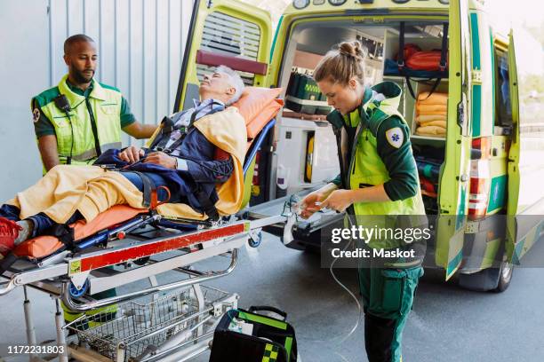 paramedic with patient looking at coworker preparing oxygen equipment outside ambulance - pessoal de ambulância imagens e fotografias de stock