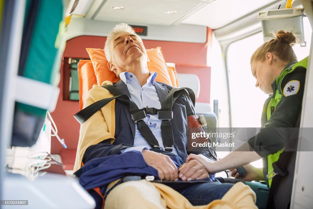 Female paramedic checking man's blood pressure in ambulance