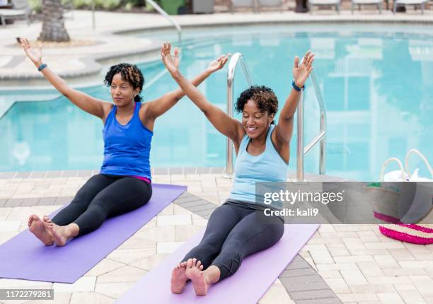identical twins sitting on yoga mats by pool, stretching - identical twin stock pictures, royalty-free photos & images