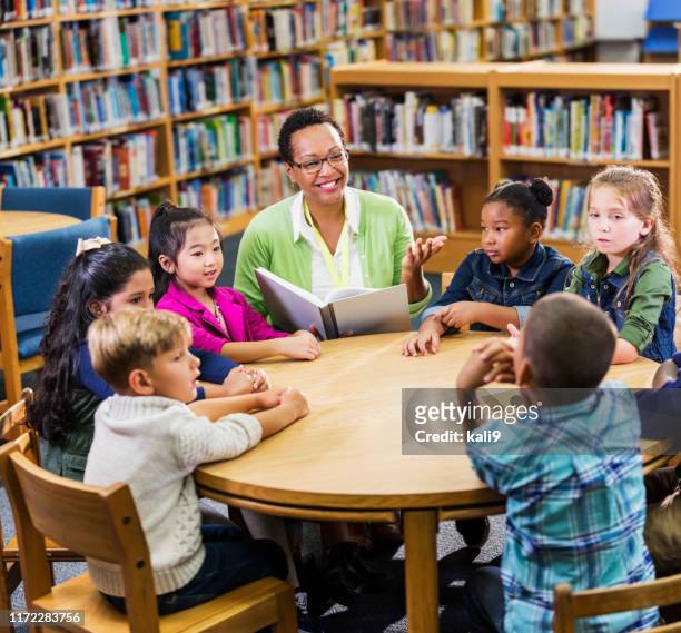 lettura insegnanti ai bambini in biblioteca - bambini seduti in cerchio foto e immagini stock