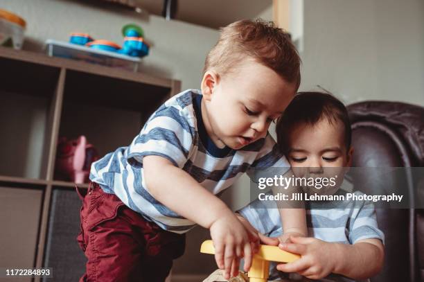 twin male toddlers play on top of a riding vintage toy in living room at home. - twin babies stockfoto's en -beelden