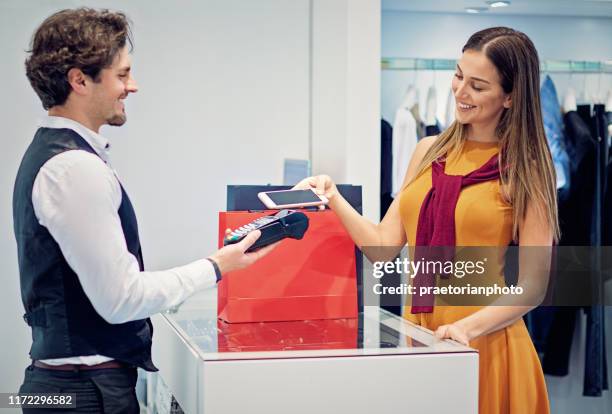 young woman is paying using mobile phone in a boutique - salesman stock pictures, royalty-free photos & images