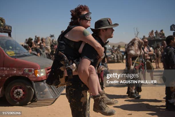 Man gives a piggy back ride to a woman during Wasteland Weekend festival at the Mojave desert in Edwards, California on September 28, 2019. - In 2019...