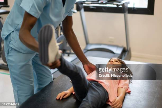 cute little girl lying down on gurney stretching her leg with help of unrecognizable physical therapist - girl lying down stock pictures, royalty-free photos & images