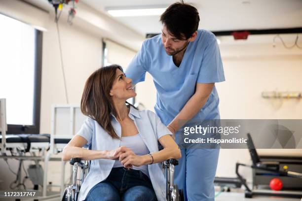 female patient on wheelchair talking to physical therapist at a rehab medical center both smiling - accident hospital stock pictures, royalty-free photos & images