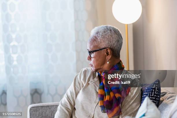 senior afro-amerikaanse vrouw kijkt door venster - casual woman pensive side view stockfoto's en -beelden
