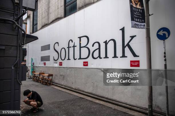 Man squats as he smokes a cigarette next to a SoftBank mobile phone store on September 30, 2019 in Tokyo, Japan. SoftBank, the technology and...